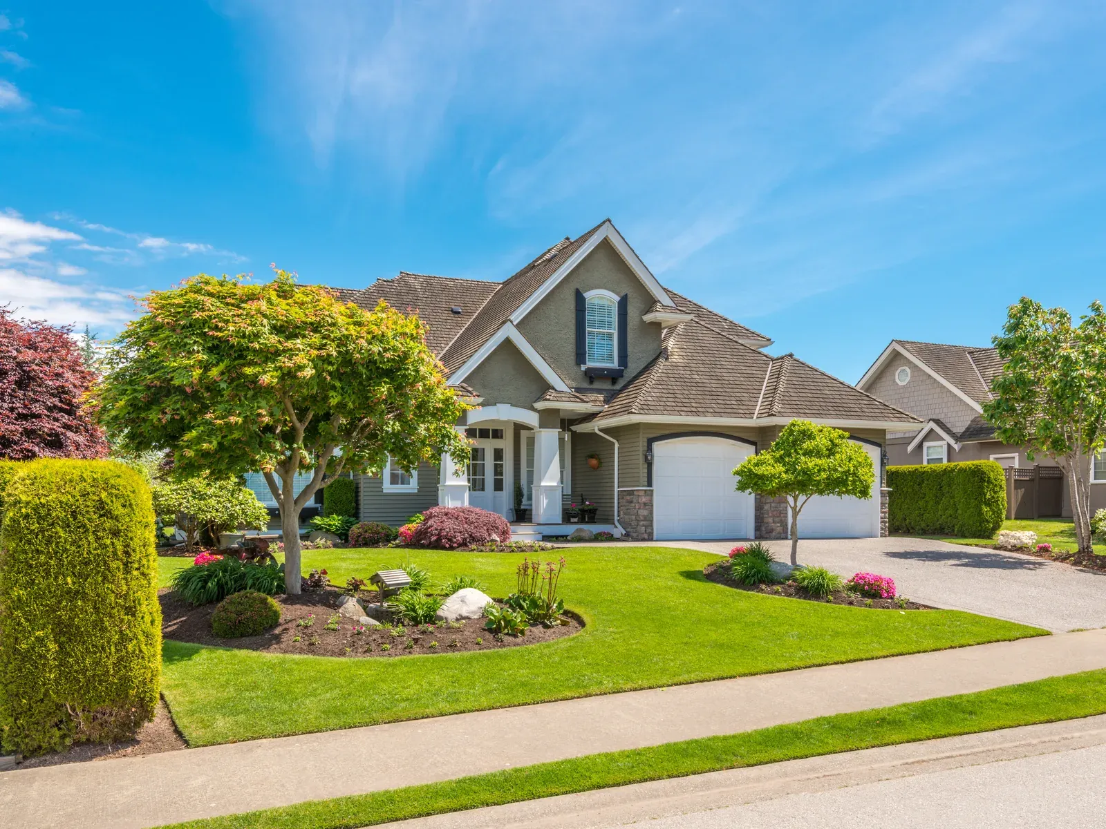 A dense, evenly green front lawn edged with trimmed hedges and flower beds in front of a suburban home